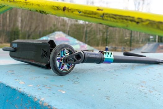 a stunt scooter, a modern extreme stunt scooter in a skate park lies on a concrete path. the scratched scooter lies after falling to the ground. The concept of a healthy lifestyle and sports leisure