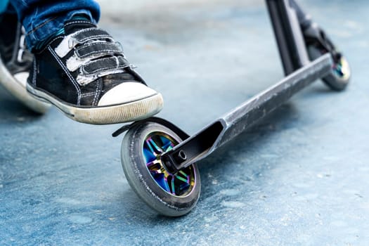 Rider boy legs close up in sneakers on stunt scooter on the skate park ramp. A boy on a scooter in a skate park performs jumps and tricks. extreme city sports outdoor Extreme jumping on a scooter. The concept of a healthy lifestyle. sports leisure