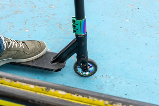 Rider boy legs close up in sneakers on stunt scooter on the skate park ramp. A boy on a scooter in a skate park performs jumps and tricks. extreme city sports outdoor Extreme jumping on a scooter. The concept of a healthy lifestyle. sports leisure