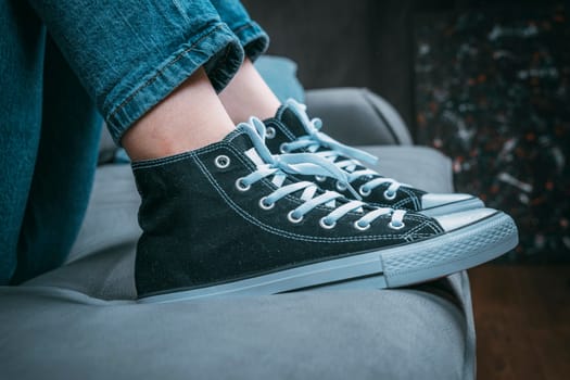 the girl's legs shod in classic sneakers. A sneakers on a girl's leg. Teenager's feet in casual new sneakers on the sofa close up image. Vintage style. concept image