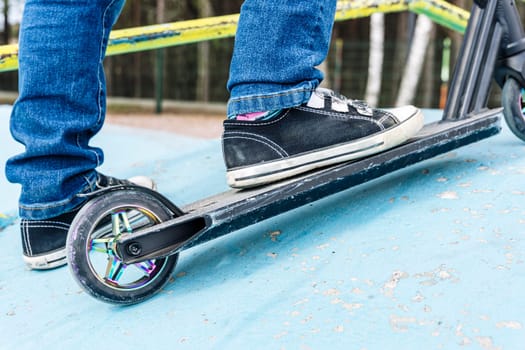 Rider boy legs close up in sneakers on stunt scooter on the skate park ramp. A boy on a scooter in a skate park performs jumps and tricks. extreme city sports outdoor Extreme jumping on a scooter. The concept of a healthy lifestyle. sports leisure