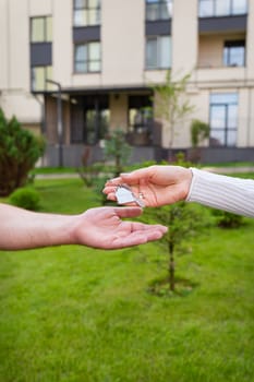 Keys with a keychain in the form of a metal house from a new house or apartment in the hands of a young family. Handing over the keys from the realtor