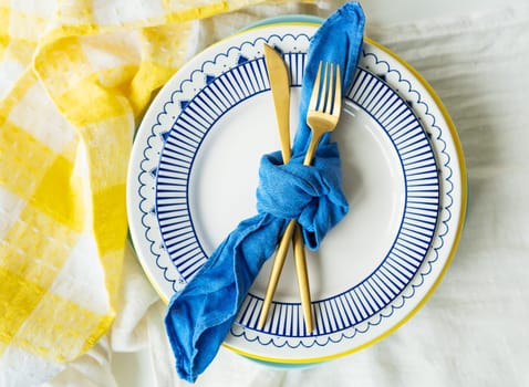 Serving design. Gold cutlery is tied with a blue napkin, on which the plates are on a yellow linen napkin. Minimalistic design, rustic