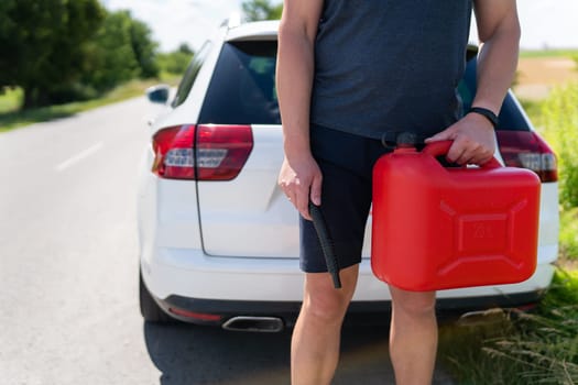 A man is holding a red can next to a white car. Stop to refuel, problems on the road with refueling