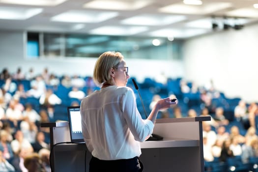 Female speaker giving a talk on corporate business conference. Unrecognizable people in audience at conference hall. Business and Entrepreneurship event