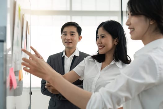 Asian business team male and female colleagues talking at work share ideas with chart on board, Happy young presenttation colleagues work together on board.