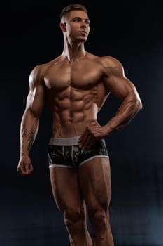 Attractive sexy bodybuilder posing in shorts in the studio on black background, demonstrating a muscular strong body. The concept of hard work in gym and body aesthetics