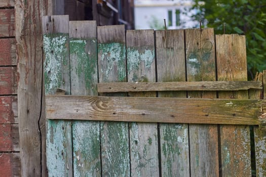 Photo of old wooden fence with faded paint. knocked out of boards. Old building. Resettlement of dilapidated fund.