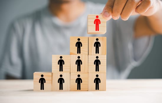 A hand carefully selecting man people icons on cube wooden toy blocks stacked. Symbolizes the connection between human resources and business success, emphasizing the role of effective management.