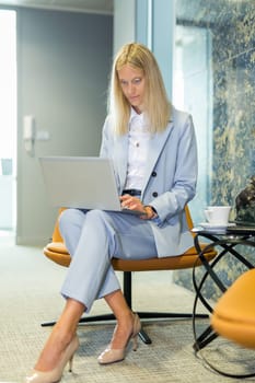 Beautiful business woman sitting at the table working on a laptop. Stylish woman in the modern office environment