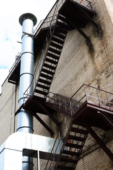 Brick wall of old factory with fire escape and metal chimney