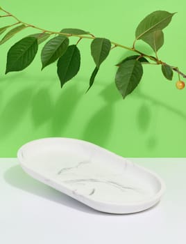 Empty oval white marble stand on a beige background and green leaves, a place to display cosmetics and products