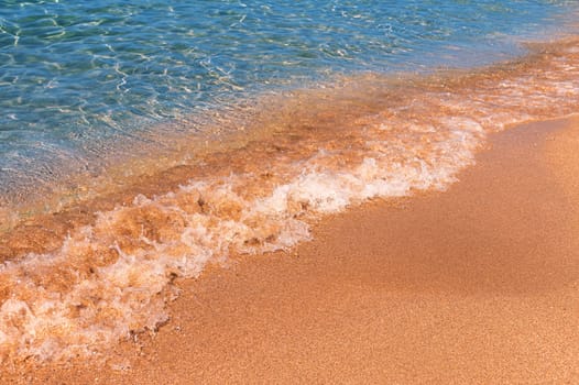 Soft sea wave on a sandy beach. Calm soft waves roll foam on the golden sandy beach.