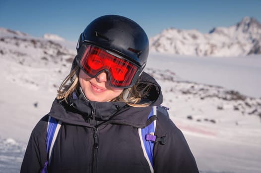 Woman skier on the slope of a mountain resort. Portrait of a young woman smiling in ski equipment, goggles and a helmet.