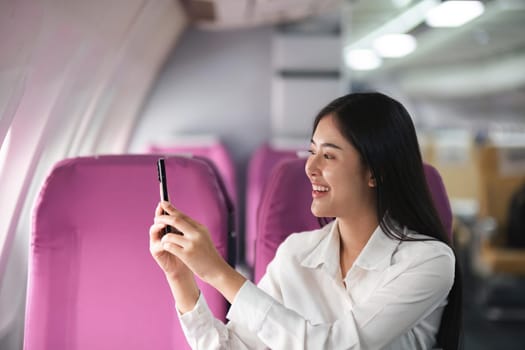 Young asian woman passenger taking photo from the window of the airplane during flight..