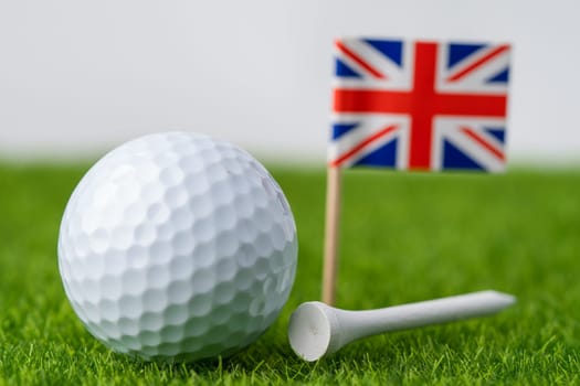 Golf ball with UK United Kingdom flag and tee on green lawn or grass is most popular sport in the world.