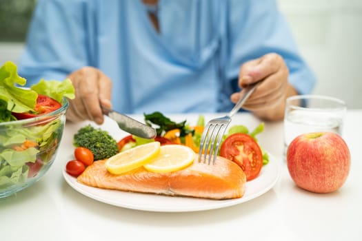 Asian elderly woman patient eating salmon steak breakfast with vegetable healthy food in hospital.