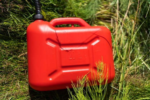 Red plastic canister among the green grass. Problems on the road with fuel for the car. High quality photo