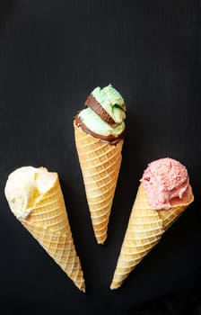 Ice cream in a waffle cone with different flavors on a black board. Vertical photo