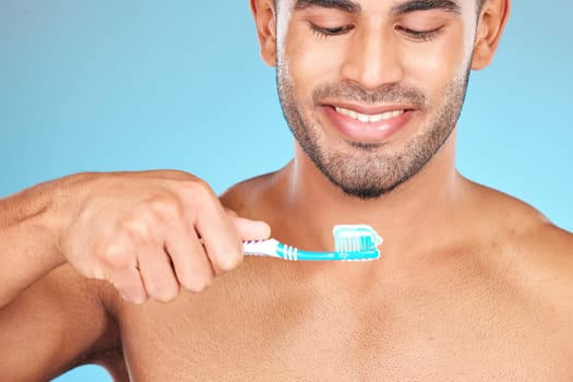 Toothbrush, toothpaste and man happy brushing teeth for dental care, morning hygiene and cleaning in studio. Smile, tooth whitening and mouth healthcare or oral care happiness in blue background.