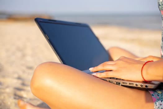 Young woman working on her laptop on the beach during sunset. Female freelancer working on the beach.