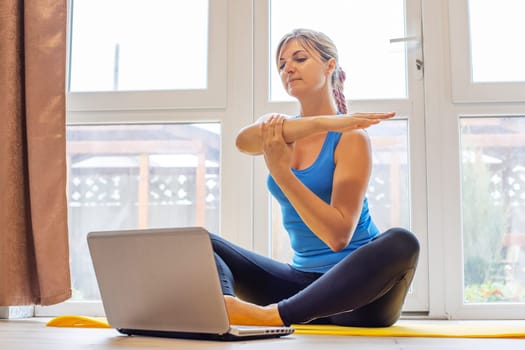 Beautiful young woman in sportswear doing sport exercises on yoga mat at home. Fitness training online with a laptop. Healthy lifestyle concept.