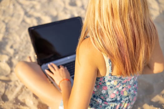 Young woman working on her laptop on the beach during sunset. Female freelancer working on the beach.