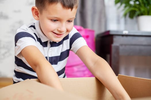 A boy is unpacking cardboard box ( gift box or parcel) at home. Delivery and service concept. Online shopping.