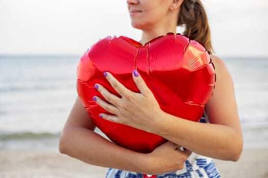 Happy young woman huging heart-shaped balloon on the beach.