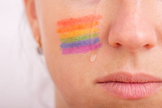 Part of the face of a young crying woman with a painted LGBT flag on her cheek. The concept of infringement of the rights and equality of LGBT people.