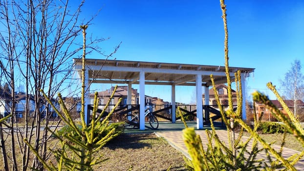 Beautiful Wooden gazebo outdoor on Sunny autumn or spring day with blue sky. Early sprint time and pavilion or alcove in village or small town on nature landscape
