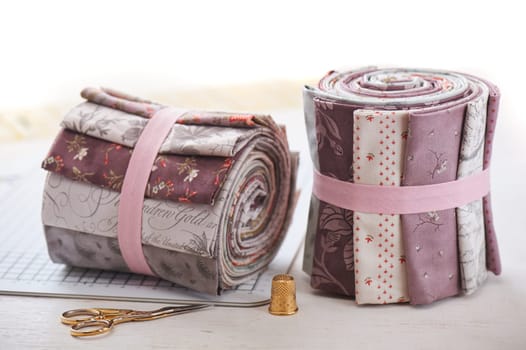 Rolls of fabric, sewing accessories on white wooden surface