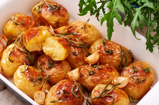Roasted potatoes with garlic, thyme and rosemary in ceramic baking dish, close-up