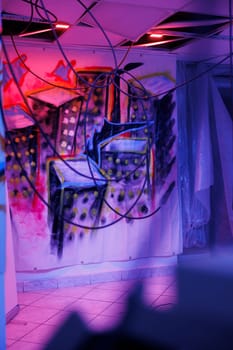 Deserted urban space with purple and pink neon lights, showing dust on walls, abandoned warehouse with crumbling structure covered in messy graffiti paint. Place with fluorescent lights.