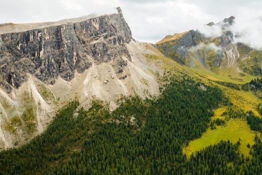Stunning image of Rocky Dolomite Alps, where the lofty peak disappears into clouds with the forest at the mountains base.