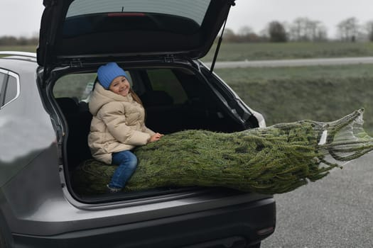 A girl sitting in the trunk with a Christmas tree