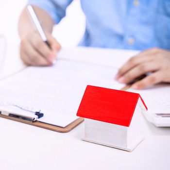 Business concept - Young Asian man in blue shirt calculates, signs agreement contract to buy a house loan payment, paying insurance, tax, close up.