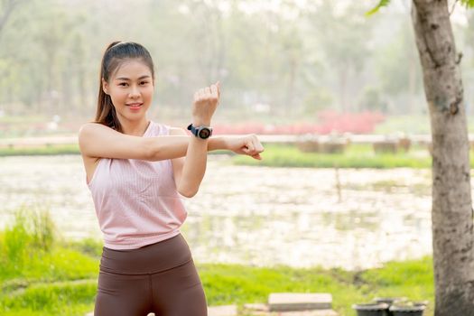 Portrait of Asian woman do arm stretching in park or garden with lake or flower field as background and morning light.