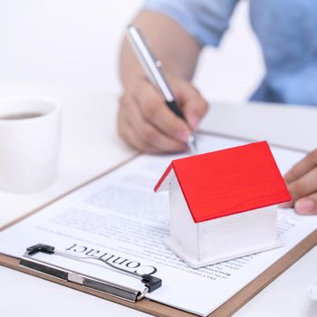 Business concept - Young Asian man in blue shirt calculates, signs agreement contract to buy a house loan payment, paying insurance, tax, close up.