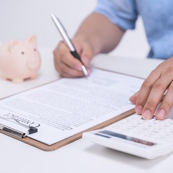 Business concept - Young Asian man in blue shirt calculates, signs agreement contract to buy a house loan payment, paying insurance, tax, close up.