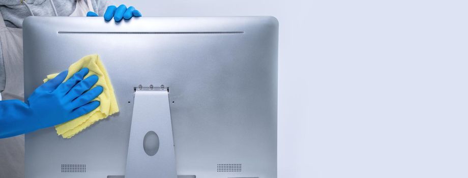 Young woman housekeeper in apron is doing cleaning silver computer screen with blue gloves, wet yellow rag, close up, copy space, blank design concept.