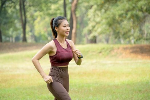Close up Asian woman jogging in park or garden with green field and tree as background during morning time.