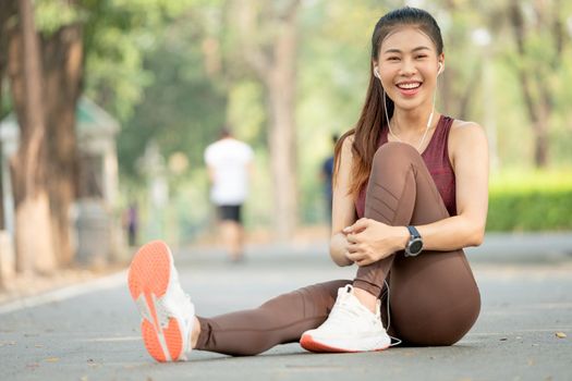 Portrait of Asian woman look at camera and sit with one's knees up on road of green park or garden with morning light.