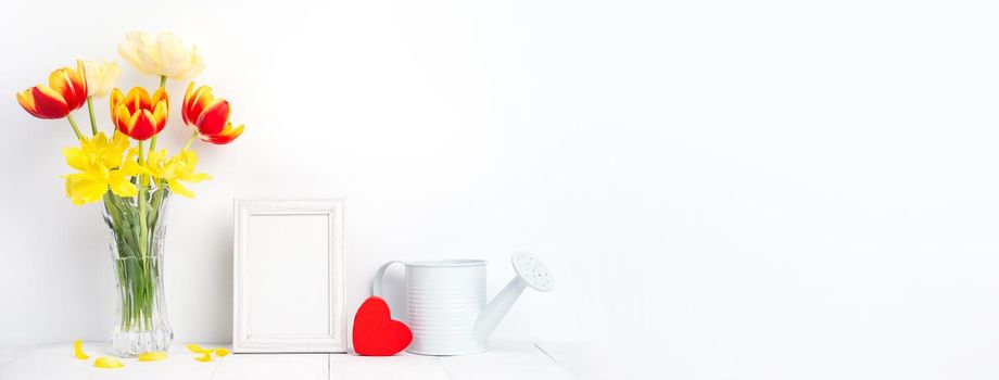 Tulip flower in glass vase with picture frame place on white wooden table background against clean wall at home, close up, Mother's Day decor concept.