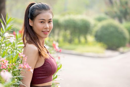 Portrait of beautiful Asian woman look at camera and stand near flower with background of road in park or garden also morning light.