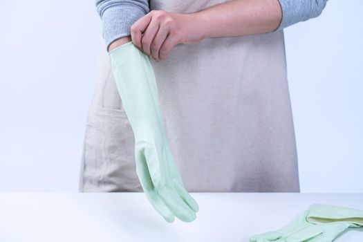 Young woman housekeeper in apron is wearing green gloves to clean the table, concept of preventing virus infection on white background, close up.