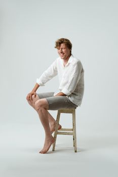 Full length of a sitting on chair smiling young man looking at camera isolated on white background. Facial expressions, emotions, feelings.