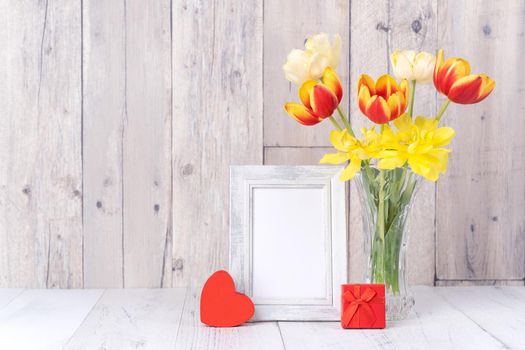 Tulip flower in glass vase with picture frame decor on wooden table background wall at home, close up, Mother's Day design concept.