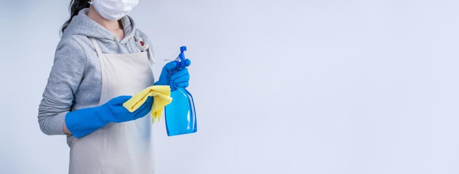Young woman housekeeper in apron is doing cleaning with blue gloves, wet yellow rag, spraying bottle cleaner, close up, copy space, blank design concept.