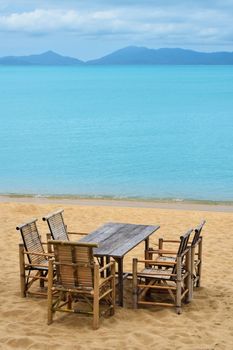 Wooden bamboo furniture, table and five chairs around on sand beach with blue sea water background in Koh Samui island, Thailand